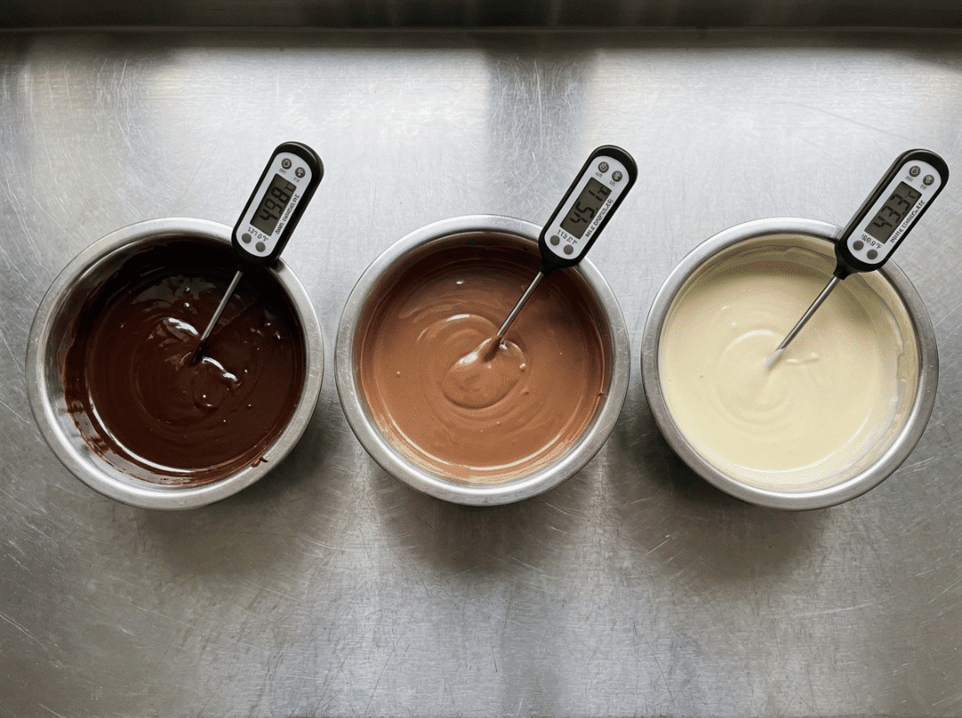 Dark, milk, and white melted chocolate with thermometers showing different melting temperatures Dark, milk, and white melted chocolate with thermometers showing different melting temperatures